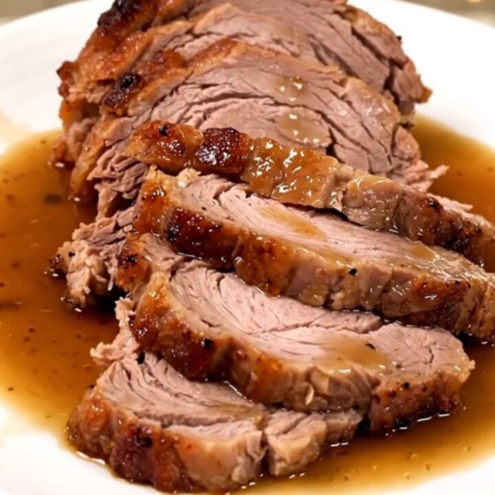 A succulent, slow-cooked pork roast served on a white plate with glossy pan juices.