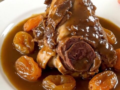 Two tender, glossy lamb shanks slow-cooked with red onions and dried apricots on a white plate.