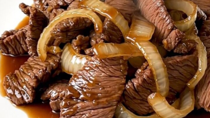 A top-down view of raw beef, sliced onions, and garlic in a black slow cooker bowl.