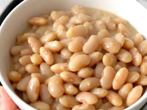 A close-up view of creamy white beans in a slow cooker topped with parmesan cheese and cream.