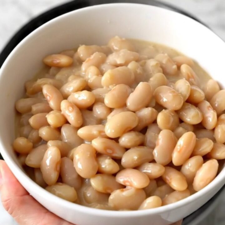 A close-up view of creamy white beans in a slow cooker topped with parmesan cheese and cream.