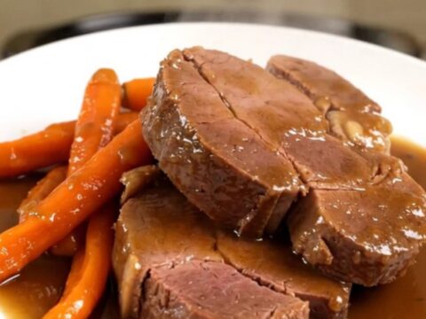 A beautifully plated braised veal shoulder roast with tender glazed carrots, ready to serve on a white plate.
