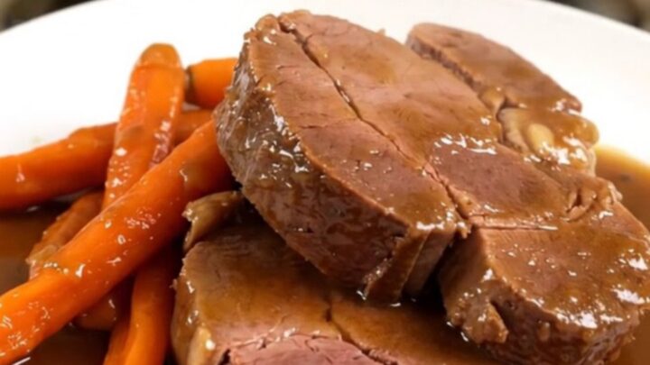 A beautifully plated braised veal shoulder roast with tender glazed carrots, ready to serve on a white plate.