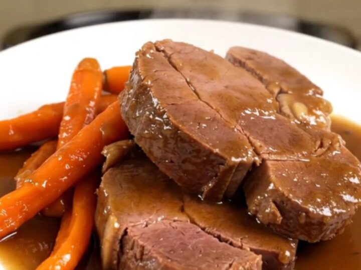 A beautifully plated braised veal shoulder roast with tender glazed carrots, ready to serve on a white plate.