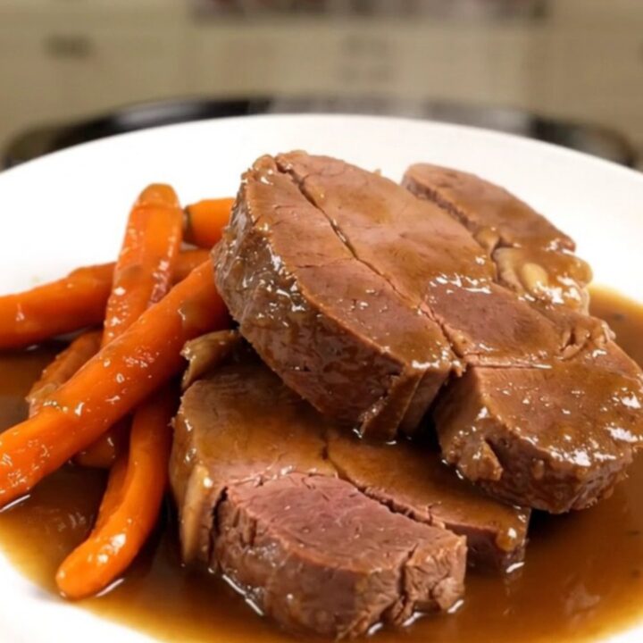 A beautifully plated braised veal shoulder roast with tender glazed carrots, ready to serve on a white plate.