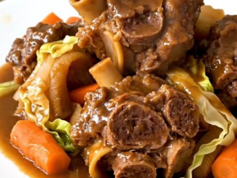 A close-up of tender, braised lamb neck slices served with vibrant carrots and shredded green cabbage in a bowl.
