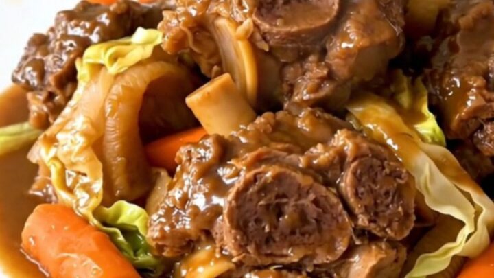 A close-up of tender, braised lamb neck slices served with vibrant carrots and shredded green cabbage in a bowl.