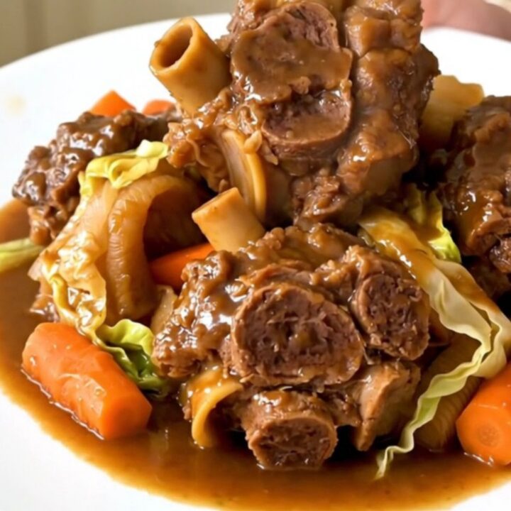 A close-up of tender, braised lamb neck slices served with vibrant carrots and shredded green cabbage in a bowl.
