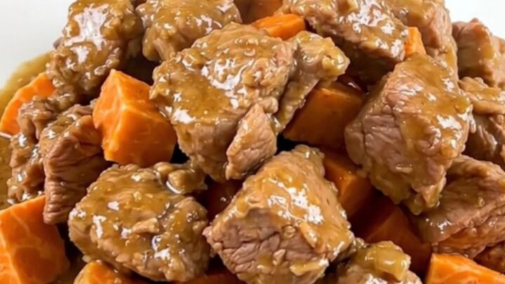A close-up of tender pork collar cubes and sweet potatoes in a creamy coconut sauce on a white plate.
