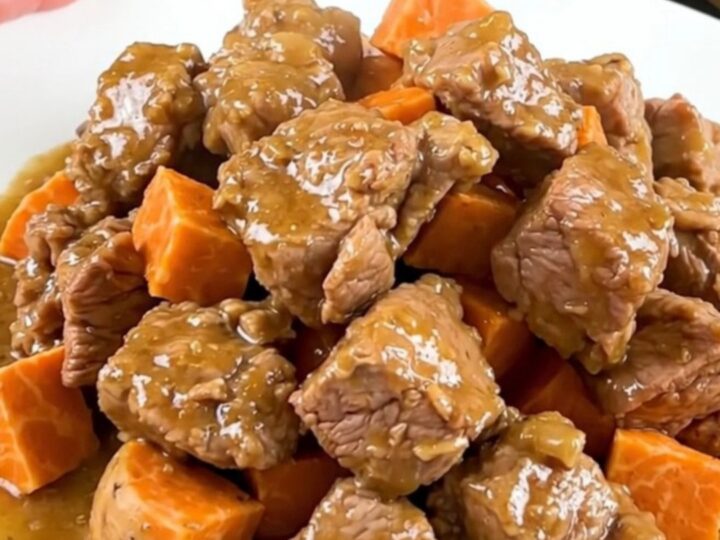 A close-up of tender pork collar cubes and sweet potatoes in a creamy coconut sauce on a white plate.