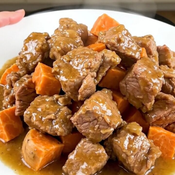A close-up of tender pork collar cubes and sweet potatoes in a creamy coconut sauce on a white plate.