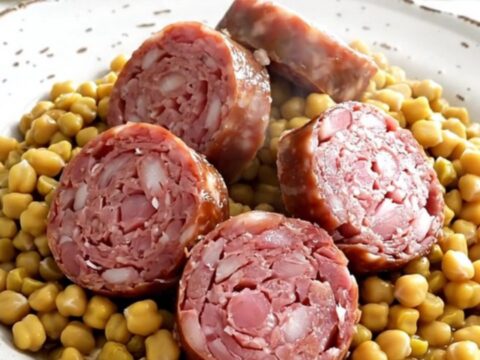 A rustic, steaming plate of sliced Morteau sausage served over a creamy mound of split peas and bright orange carrots.
