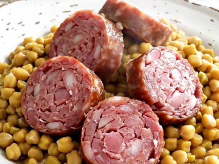 A rustic, steaming plate of sliced Morteau sausage served over a creamy mound of split peas and bright orange carrots.