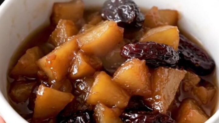 A white ceramic bowl filled with warm, glossy slow-cooked apple and prune compote in a rustic kitchen.