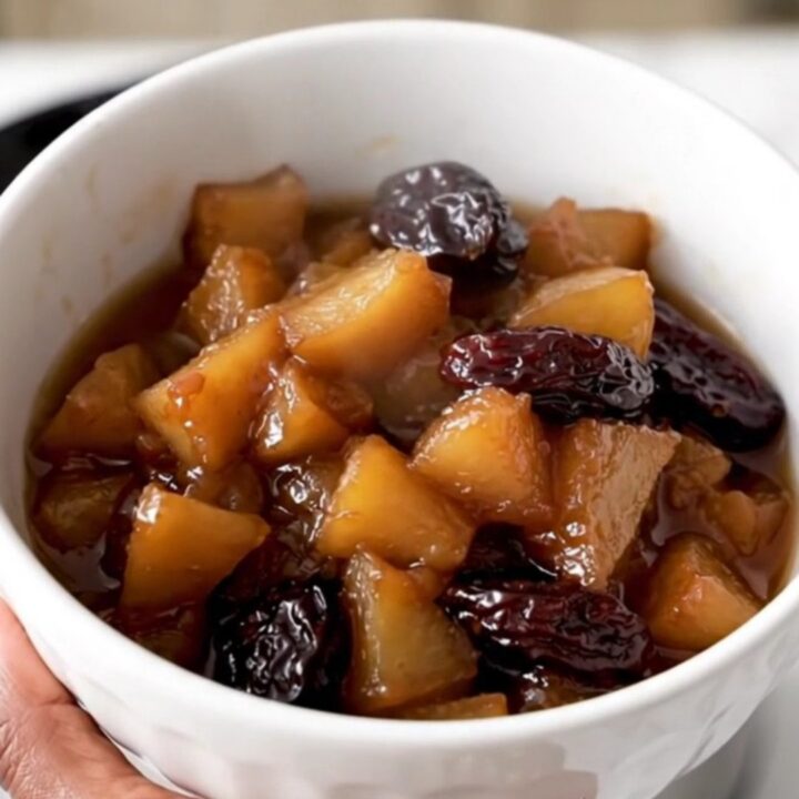 A white ceramic bowl filled with warm, glossy slow-cooked apple and prune compote in a rustic kitchen.