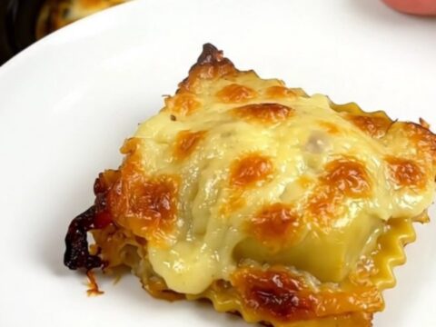A top-down view of a slow cooker filled with layers of ravioli, ham, and melted Comté cheese.