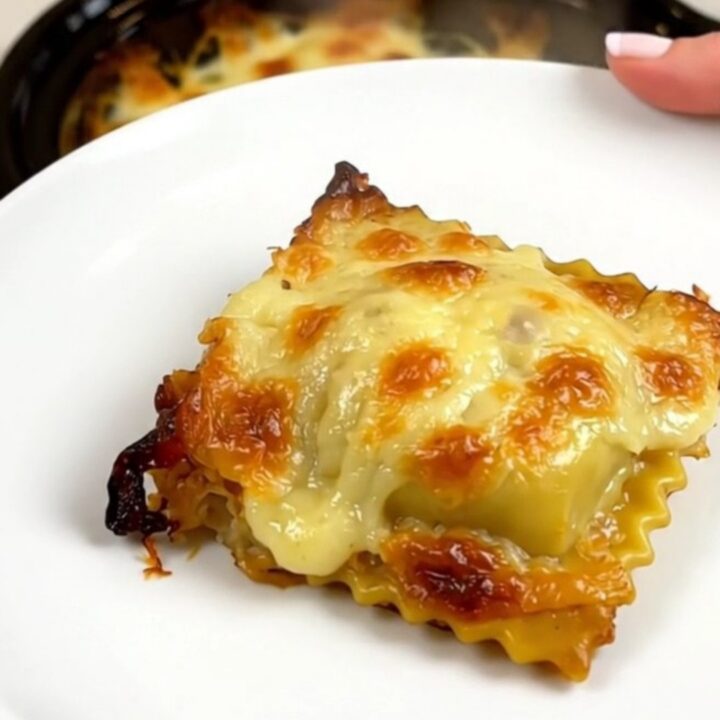 A top-down view of a slow cooker filled with layers of ravioli, ham, and melted Comté cheese.