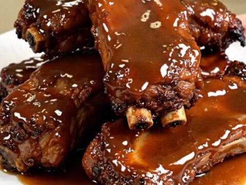 A close-up of tender, glazed maple mustard pork ribs served on a clean white plate.