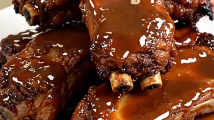 A close-up of tender, glazed maple mustard pork ribs served on a clean white plate.