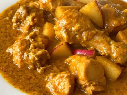 A top-down view of a slow cooker filled with chicken, apples, and onions before cooking.