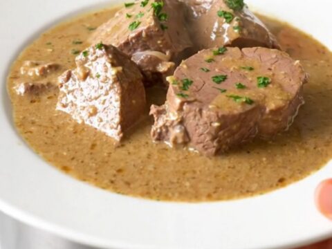 A steaming, creamy veal stew served on a white plate in a bright, modern kitchen setting.