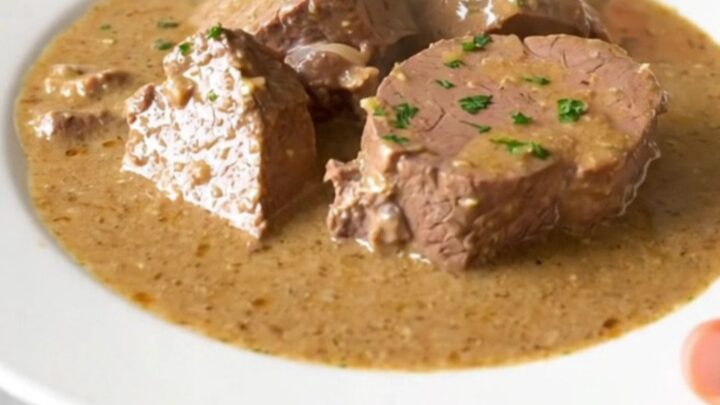 A steaming, creamy veal stew served on a white plate in a bright, modern kitchen setting.