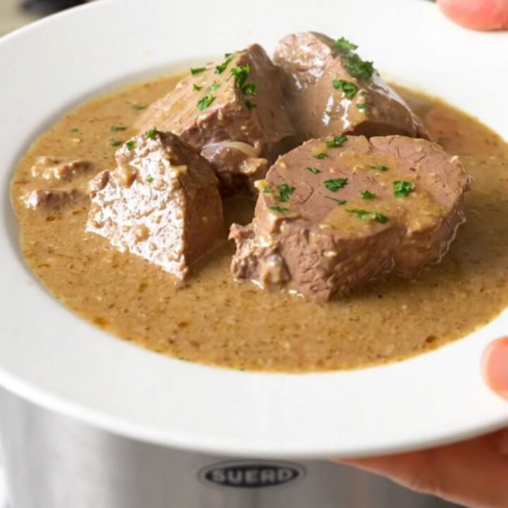 A steaming, creamy veal stew served on a white plate in a bright, modern kitchen setting.