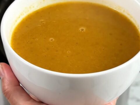 A white ceramic bowl filled with velvety, golden pumpkin and red lentil soup, steaming gently.