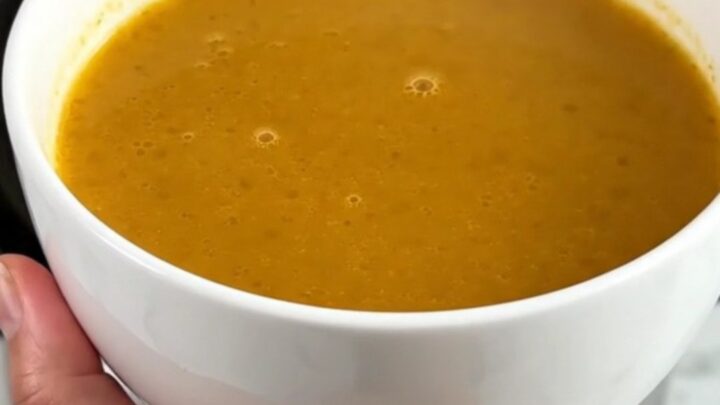 A white ceramic bowl filled with velvety, golden pumpkin and red lentil soup, steaming gently.