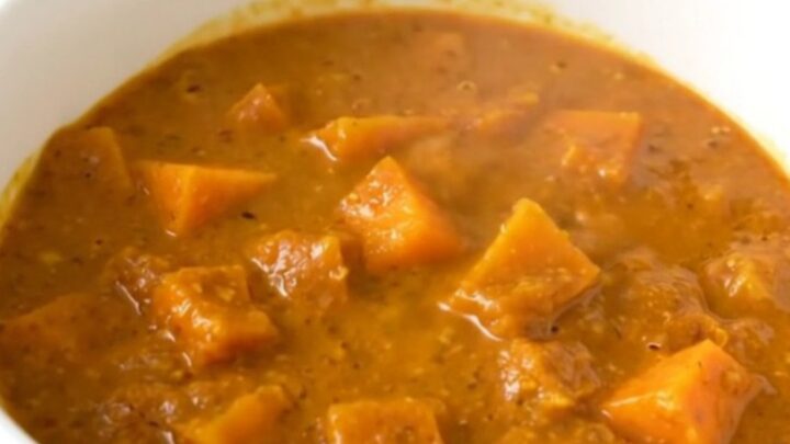 A top-down view of a black slow cooker filled with raw red lentils, diced butternut squash, and coconut milk.