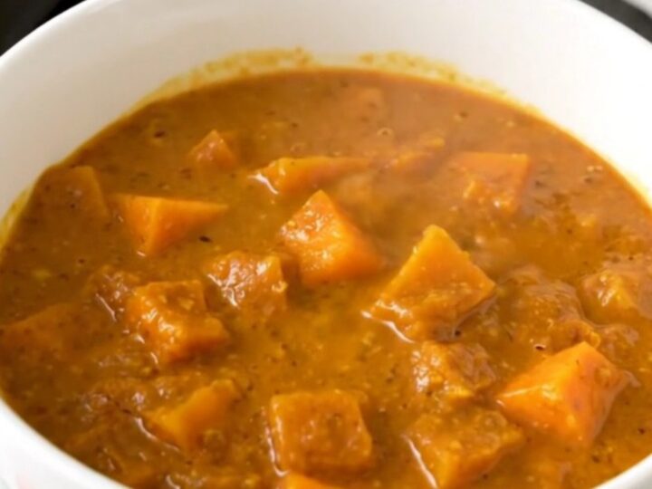 A top-down view of a black slow cooker filled with raw red lentils, diced butternut squash, and coconut milk.
