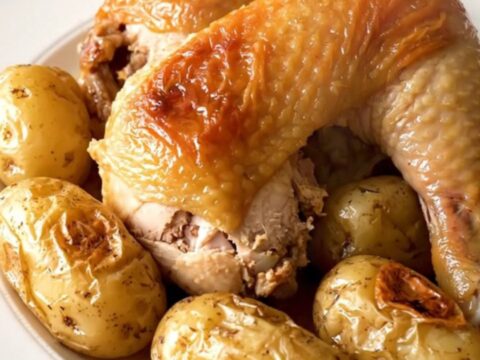 A close-up of slow-cooked chicken drumsticks and baby potatoes in a savory herb broth served on a white plate.
