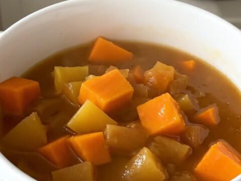 A white bowl filled with glossy, steaming autumn vegetable stew featuring pumpkin, carrots, and leeks.