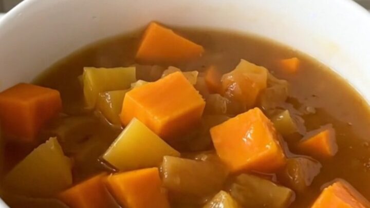 A white bowl filled with glossy, steaming autumn vegetable stew featuring pumpkin, carrots, and leeks.