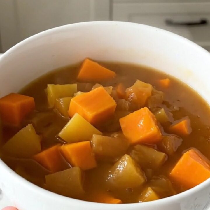 A white bowl filled with glossy, steaming autumn vegetable stew featuring pumpkin, carrots, and leeks.