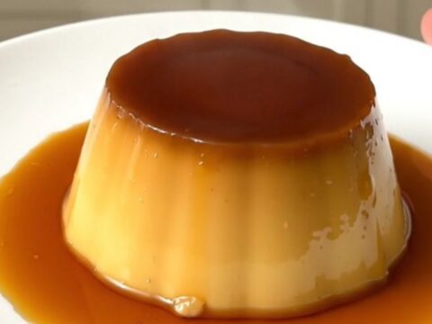 A finished coffee crème caramel unmolded on a white plate with glossy amber syrup.