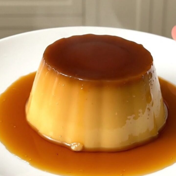 A finished coffee crème caramel unmolded on a white plate with glossy amber syrup.