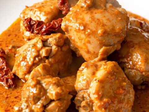 A top-down view of a slow cooker filled with raw chicken breasts, sliced sun-dried tomatoes, and a creamy mascarpone sauce.