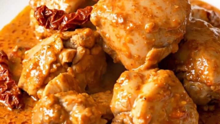 A top-down view of a slow cooker filled with raw chicken breasts, sliced sun-dried tomatoes, and a creamy mascarpone sauce.