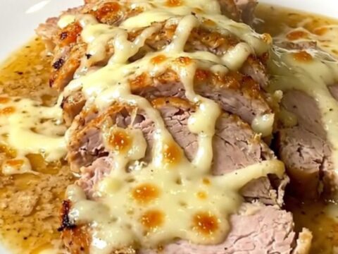 A plate of sliced, tender pork loin covered in a creamy white sauce on a white plate.
