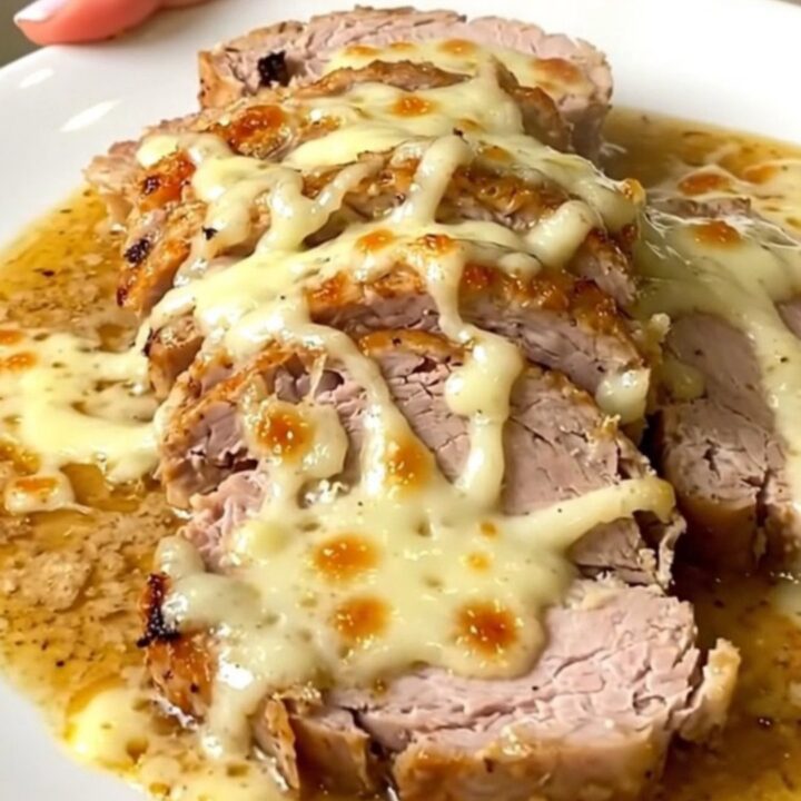 A plate of sliced, tender pork loin covered in a creamy white sauce on a white plate.