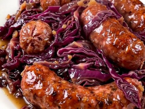 Vue de dessus d'une mijoteuse remplie de chou rouge, saucisses et pommes.