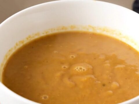 A close-up of a creamy, light-brown chestnut and porcini velouté served in a white ceramic bowl.