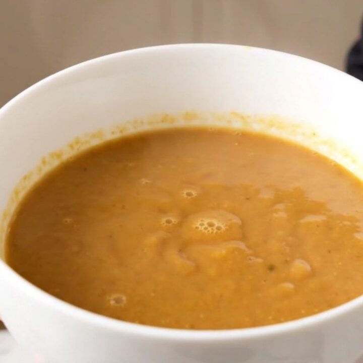 A close-up of a creamy, light-brown chestnut and porcini velouté served in a white ceramic bowl.
