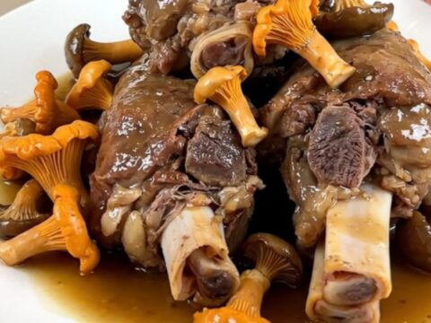 Slow cooked veal shanks with marrow bone and chanterelle mushrooms in a dark oval slow cooker.
