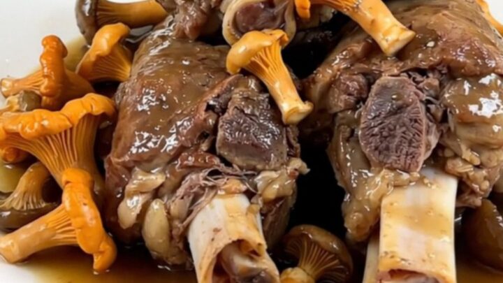 Slow cooked veal shanks with marrow bone and chanterelle mushrooms in a dark oval slow cooker.