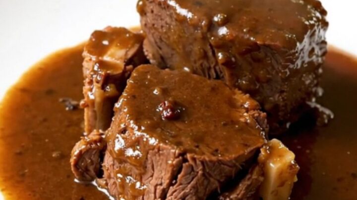A slow cooker filled with braised beef, carrots, and rosemary on a kitchen counter.
