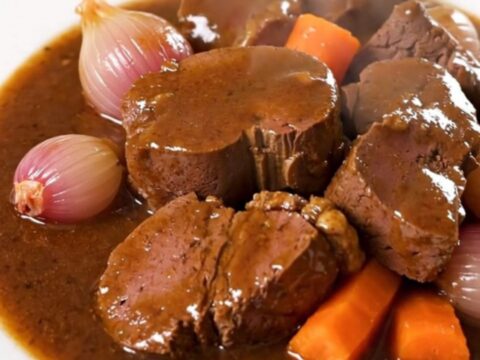 A glossy, rich Bordelaise veal stew served on a white plate with visible carrots and shallots.