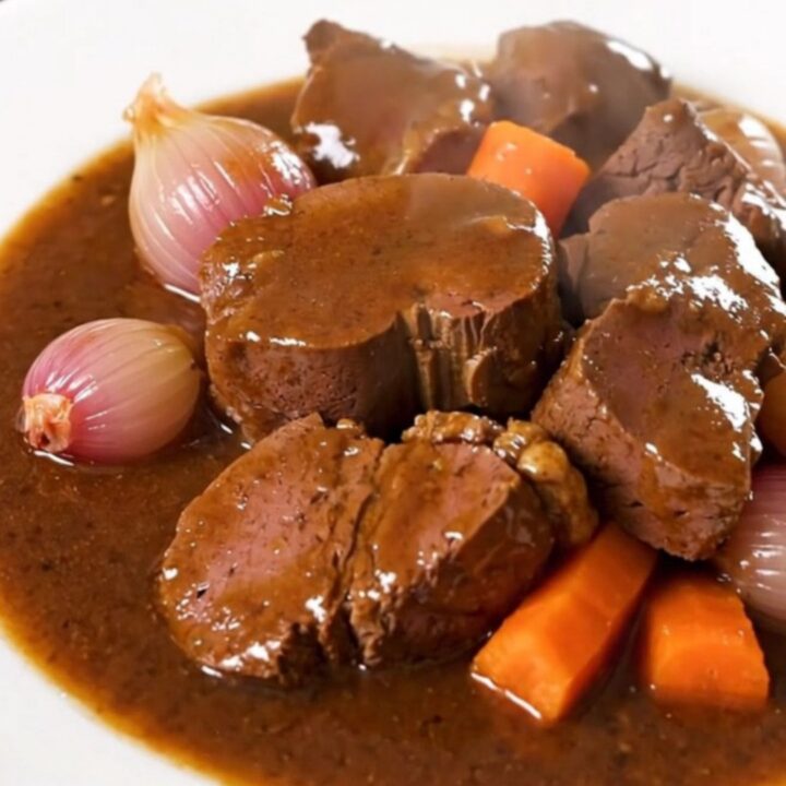 A glossy, rich Bordelaise veal stew served on a white plate with visible carrots and shallots.