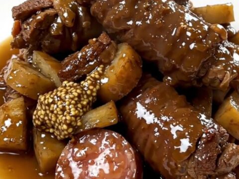 A top-down view of a slow cooker filled with sliced andouille sausage, chunks of potatoes, and carrots.